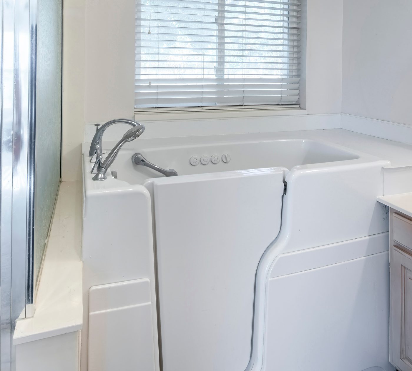 Walk-in bathtub with a hinged, sealed door, a low step-in and a handheld shower at the tap