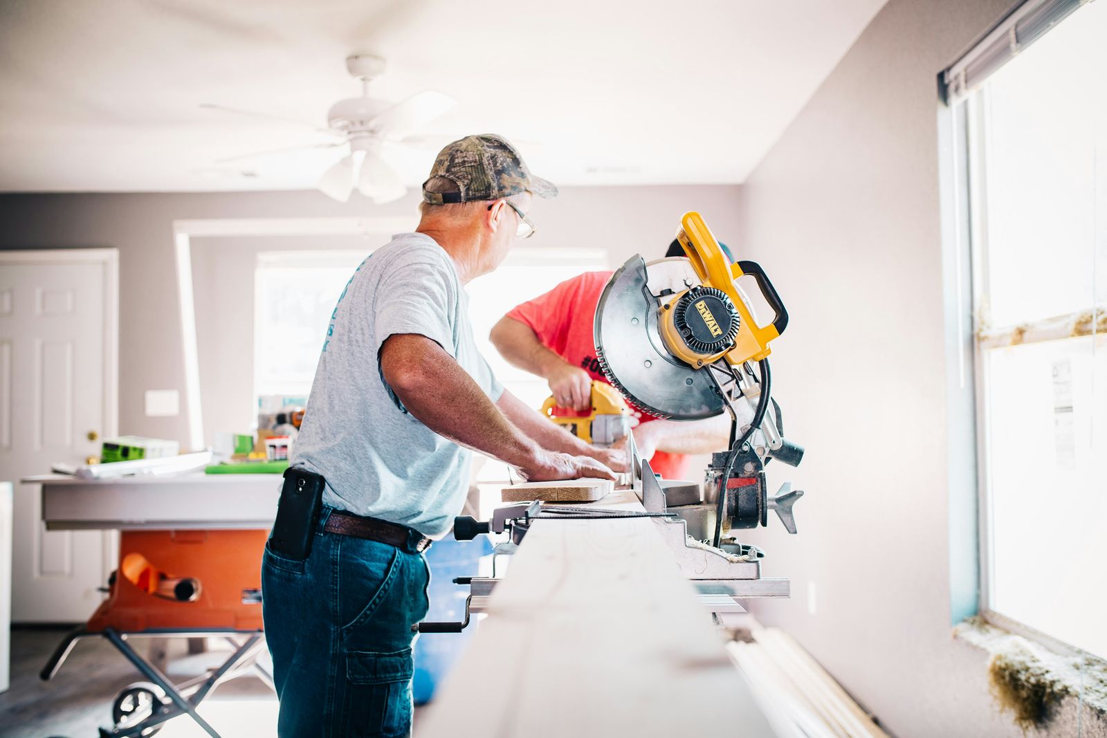 Two carpenters cutting trim on a miter saw inside a room under renovation